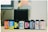 A row of eight film canisters are aligned on a surface. The canisters feature various colorful labels from different brands, including Agfa Vista, CVS Color Film, and Ilford Pan. The background appears slightly blurred with neutral tones, indicating a focus on the film canisters.