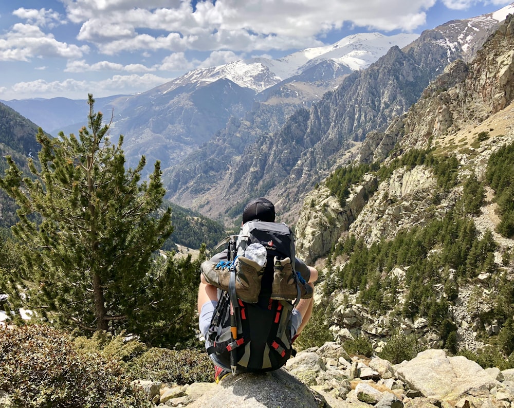 Mann sitzt auf Klippe und schaut tagsüber auf Berge und Bäume