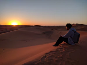 A warm sunset over the golden Sahara dunes with a lone traveler admiring the view