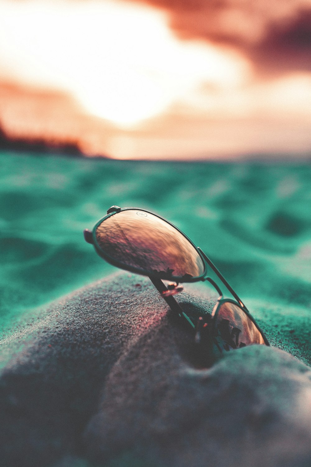 close up photography of black Aviator-style sunglasses on gray sand