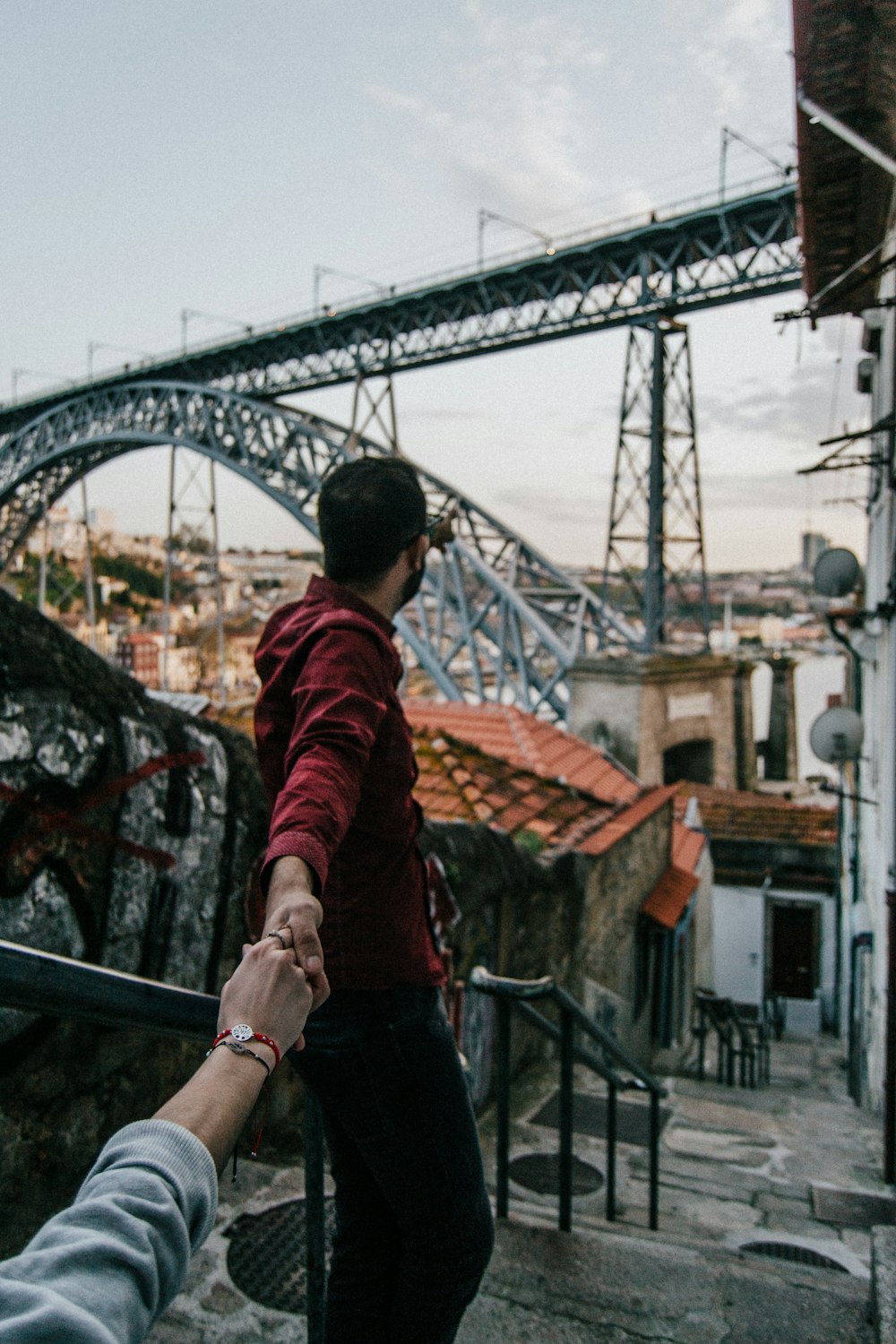 man and woman holding hands standing on stairs near bridge during daytime