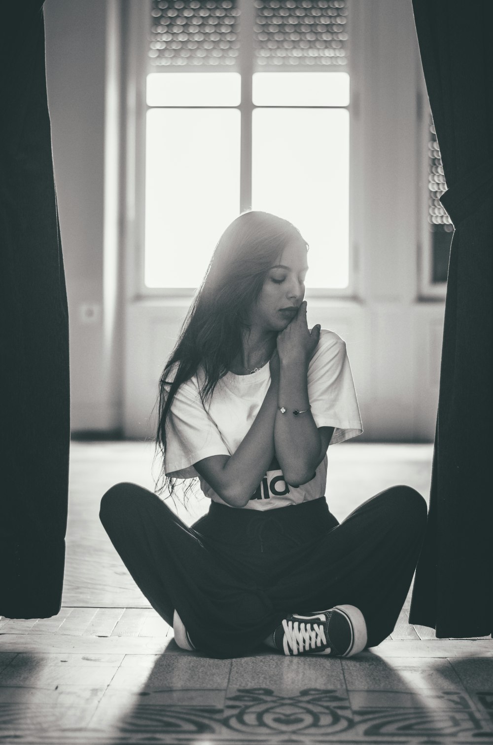 gray scale photography of woman sitting near between curtain