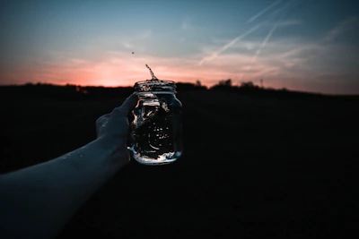 A hand gently holding the glass jar against a backdrop of Ibiza’s sparkling coastline at sunset.