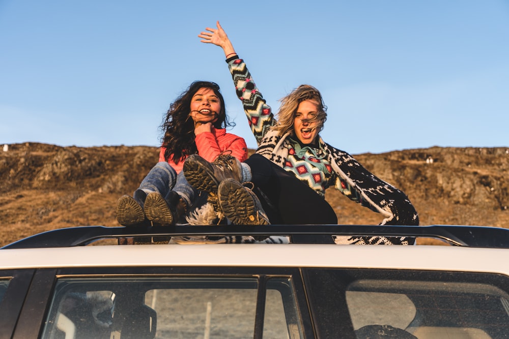 two woman sitting on top of white vehicle under blue sky during daytime