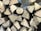 A stack of chopped wooden logs arranged in a neat pile. The logs have a visible, freshly cut appearance with light brown hues and distinct growth rings and textures.