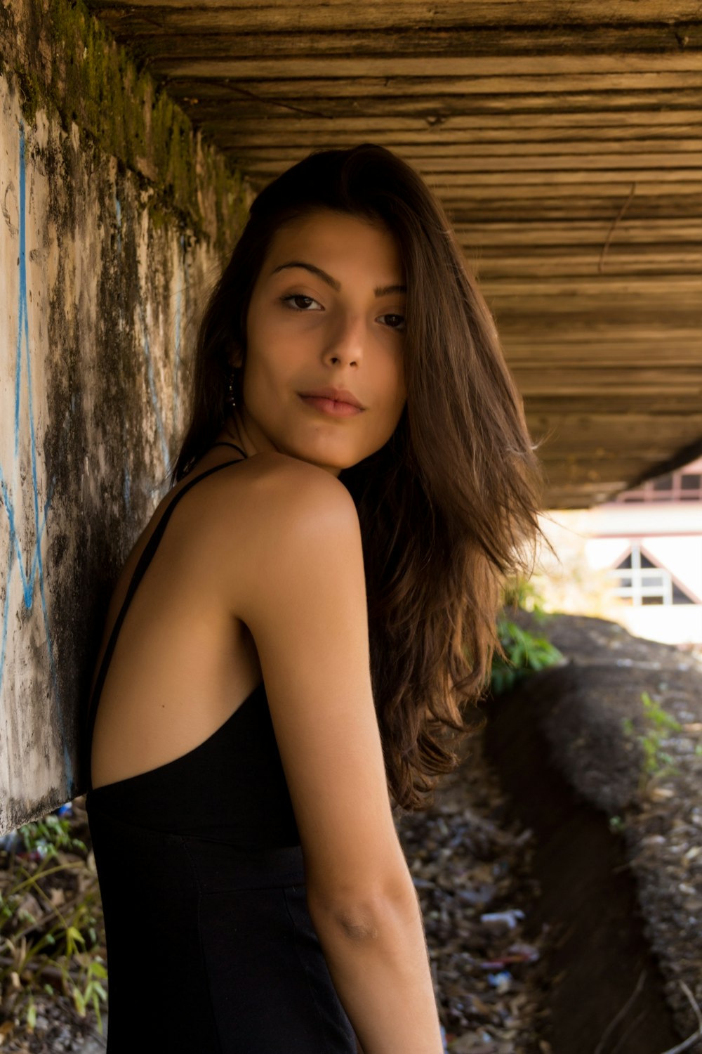 woman wearing black cami top leaning on wall under boardwalk