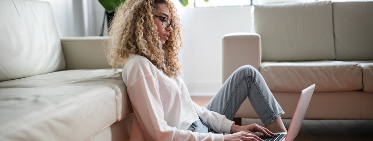 woman sitting on floor and leaning on couch using laptop