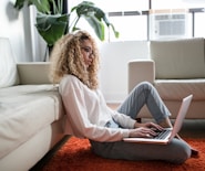 woman sitting on floor and leaning on couch using laptop