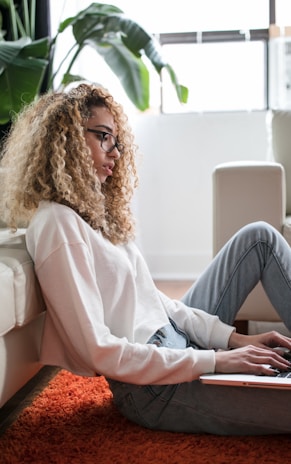 woman sitting on floor and leaning on couch using laptop