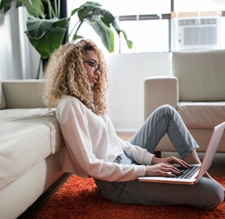 woman sitting on floor and leaning on couch using laptop