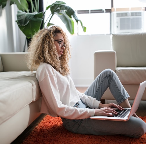 woman sitting on floor and leaning on couch using laptop