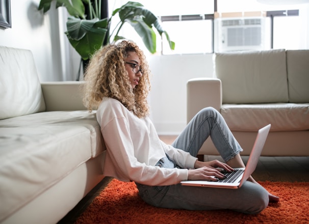 woman sitting on floor and leaning on couch using laptop