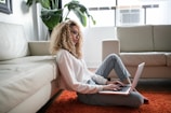 woman sitting on floor and leaning on couch using laptop