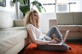 woman sitting on floor and leaning on couch using laptop