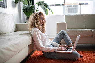 woman sitting on floor and leaning on couch using laptop