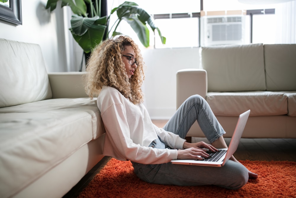 Donna seduta sul pavimento e appoggiata sul divano usando il computer portatile