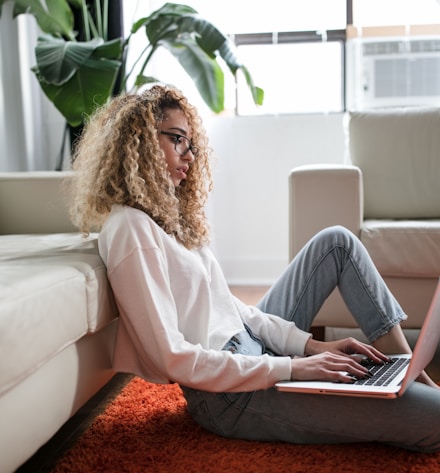 woman sitting on floor and leaning on couch using laptop