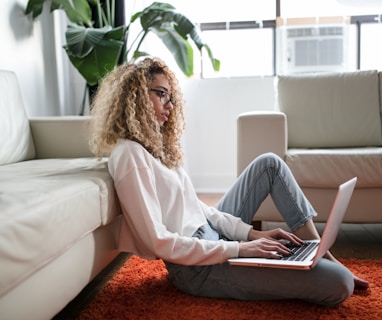 woman sitting on floor and leaning on couch using laptop