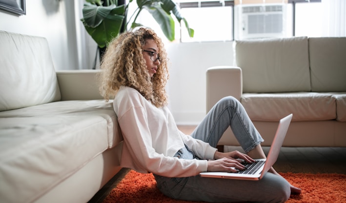 woman sitting on floor and leaning on couch using laptop