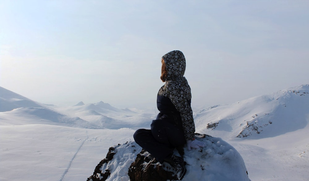 person sitting on rock formation covered by snow