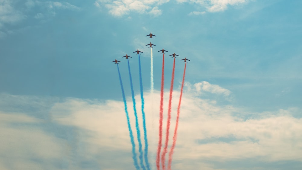 blue, red, and white aircraft in flight creating contrails