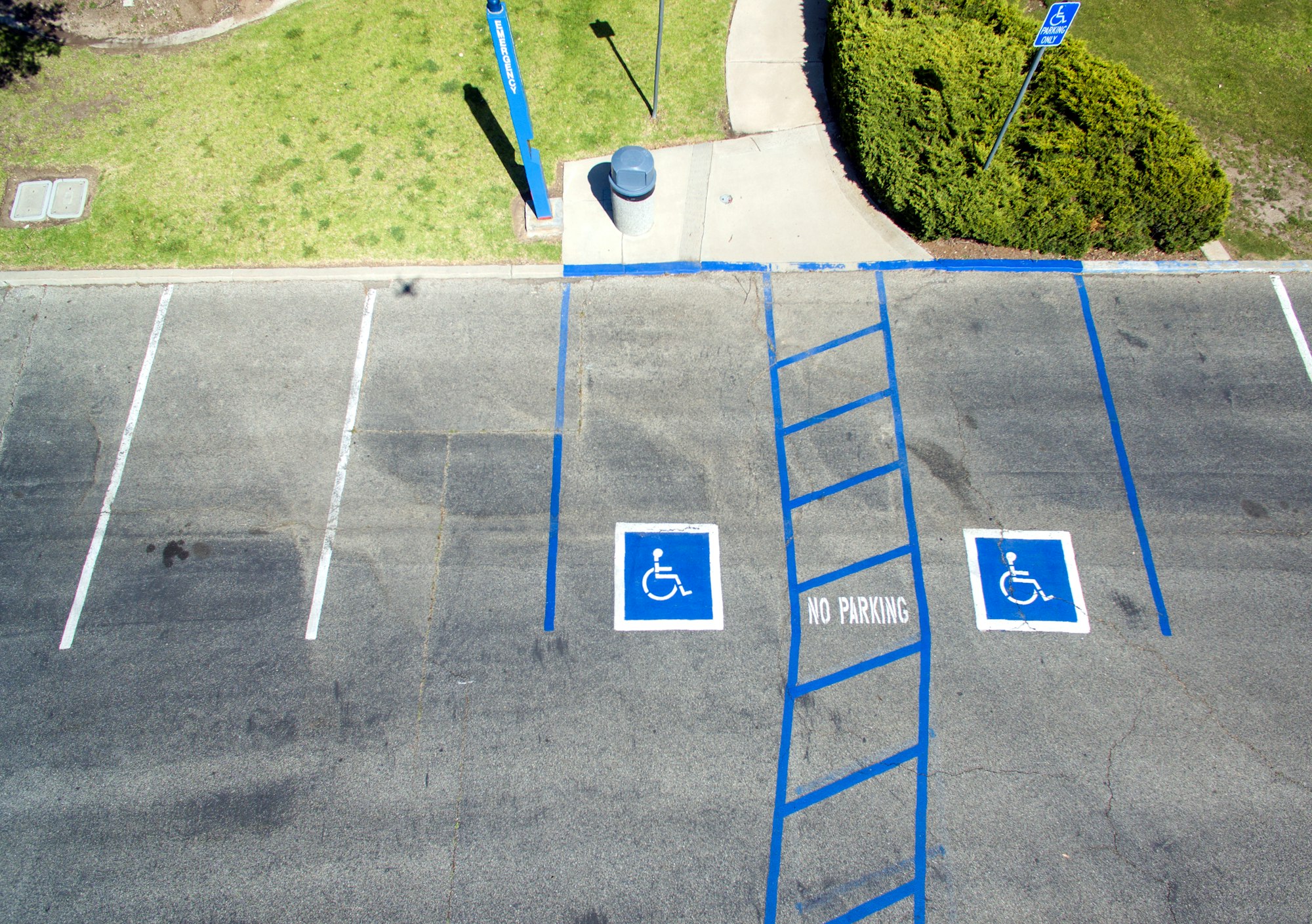 A drone photo of two wheelchair parking lots in front of a dropped curb. The parking spots are marked in blue.
