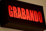 A red illuminated sign displaying the word 'GRABANDO' in bold uppercase letters against a dark background. The lighting suggests it is a signal for recording in progress.