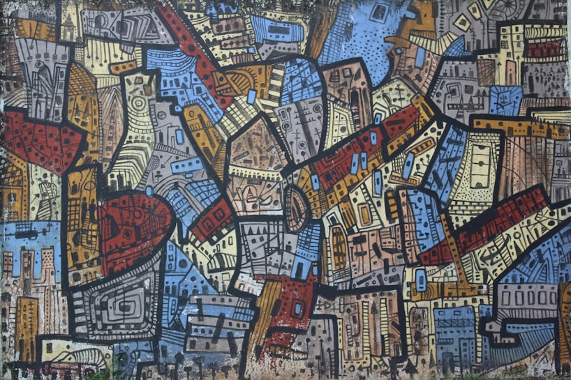 A vibrant, abstract mural featuring a busy composition of geometric shapes and patterns in varying colors. The artwork is densely packed with rectangles, triangles, and other forms, all outlined in bold black lines. The design is reminiscent of a cityscape with a blend of earthy and cool tones.