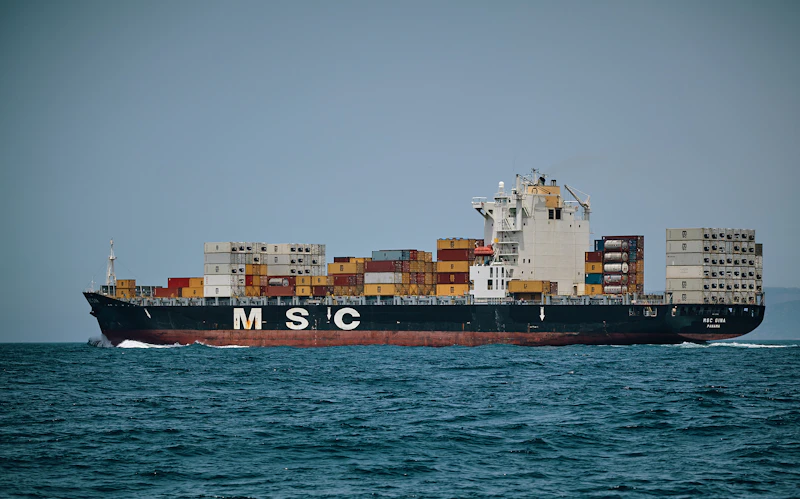 Tanker vessel navigating through a narrow strait at sunset with mountainous coastline