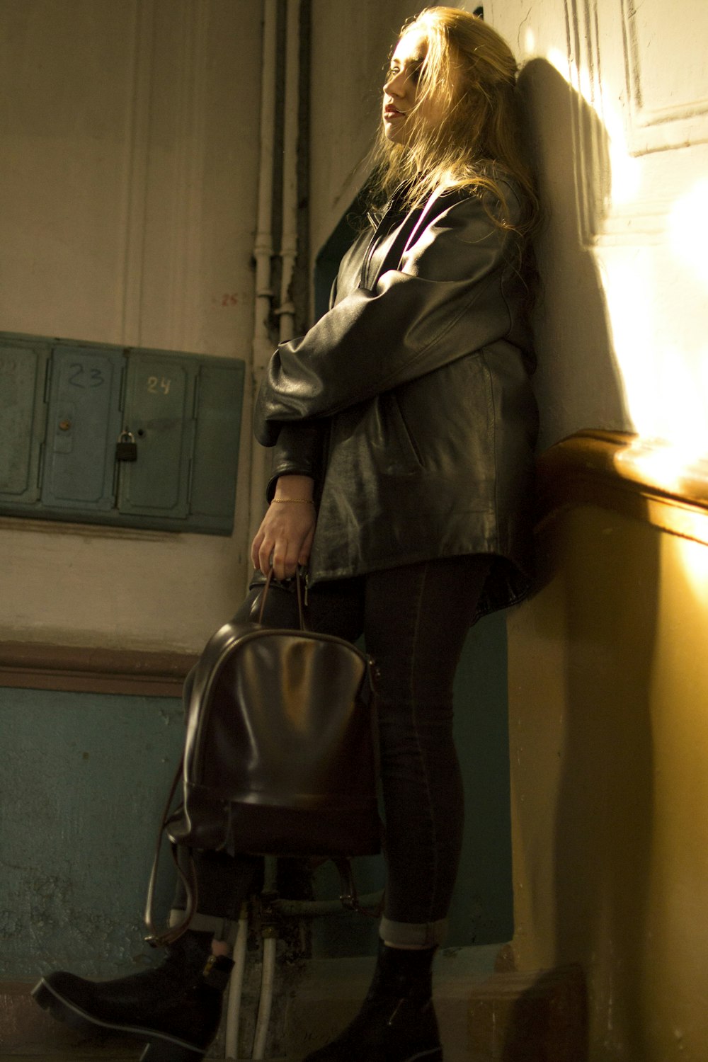 woman carrying bag while leaning on wall