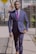 man in blue suit walking on the sidewalk near metal fence and parked vehicle