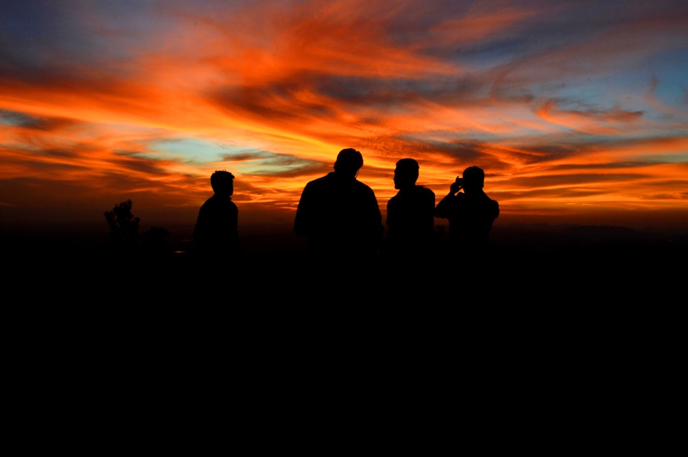Silhouette von vier Personen unter orangefarbenem Himmel