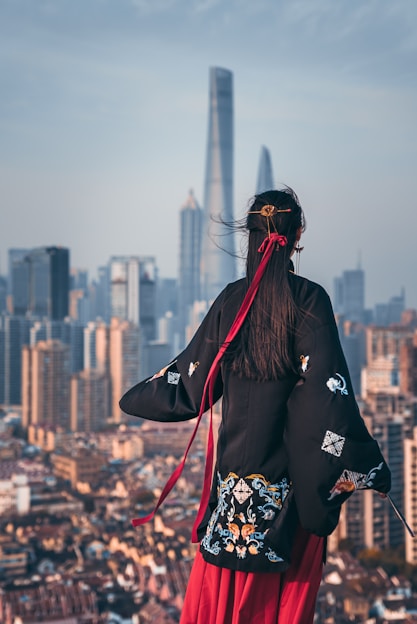 black haired woman in black coat staring at building during daytime