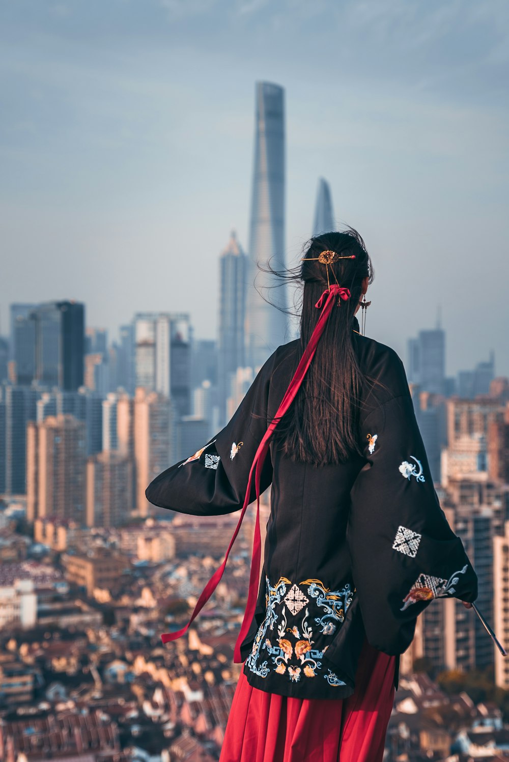 black haired woman in black coat staring at building during daytime