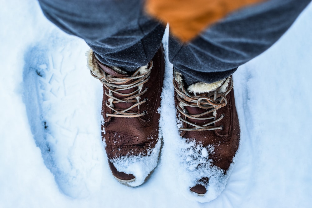 Person, die in braunen Stiefeln auf Schnee steht