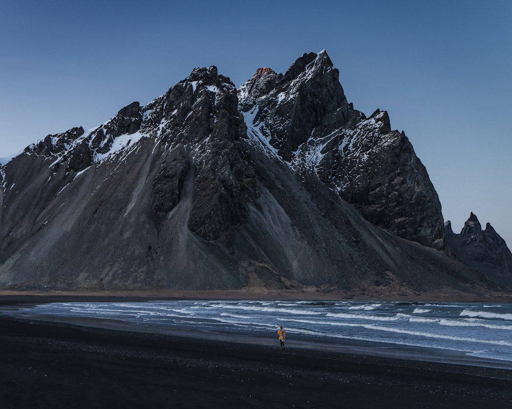 person walking on shoreline with mountain as background