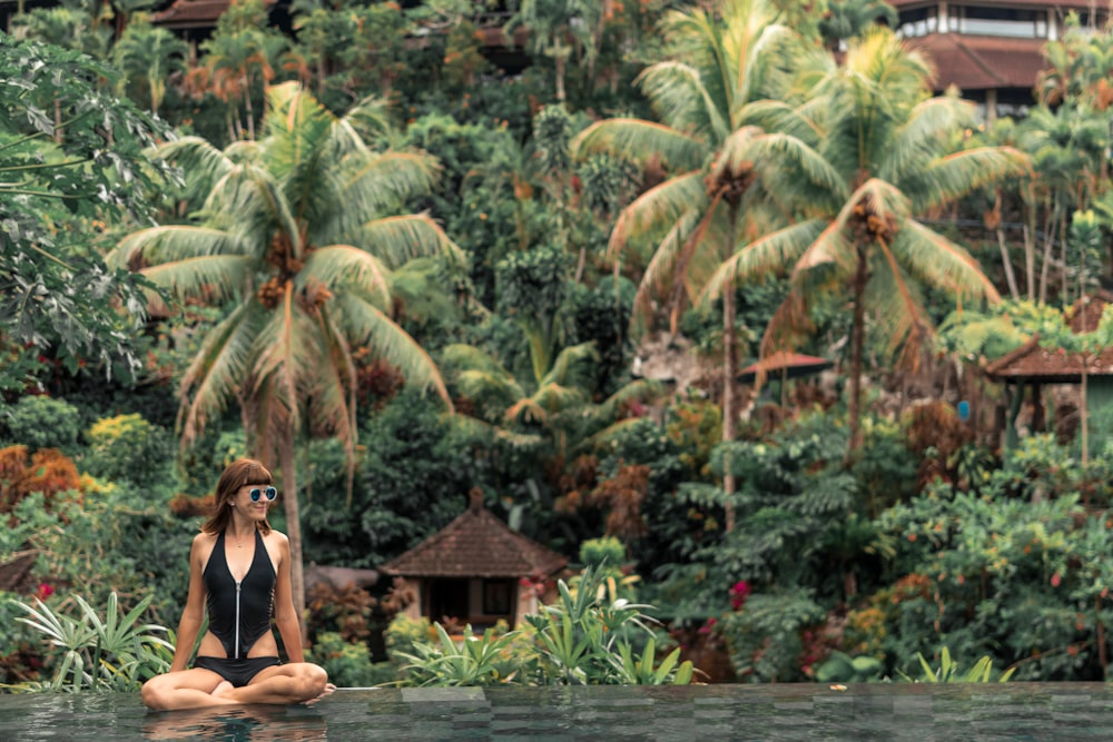 woman in black swimsuit sitting near green palm tree during daytime