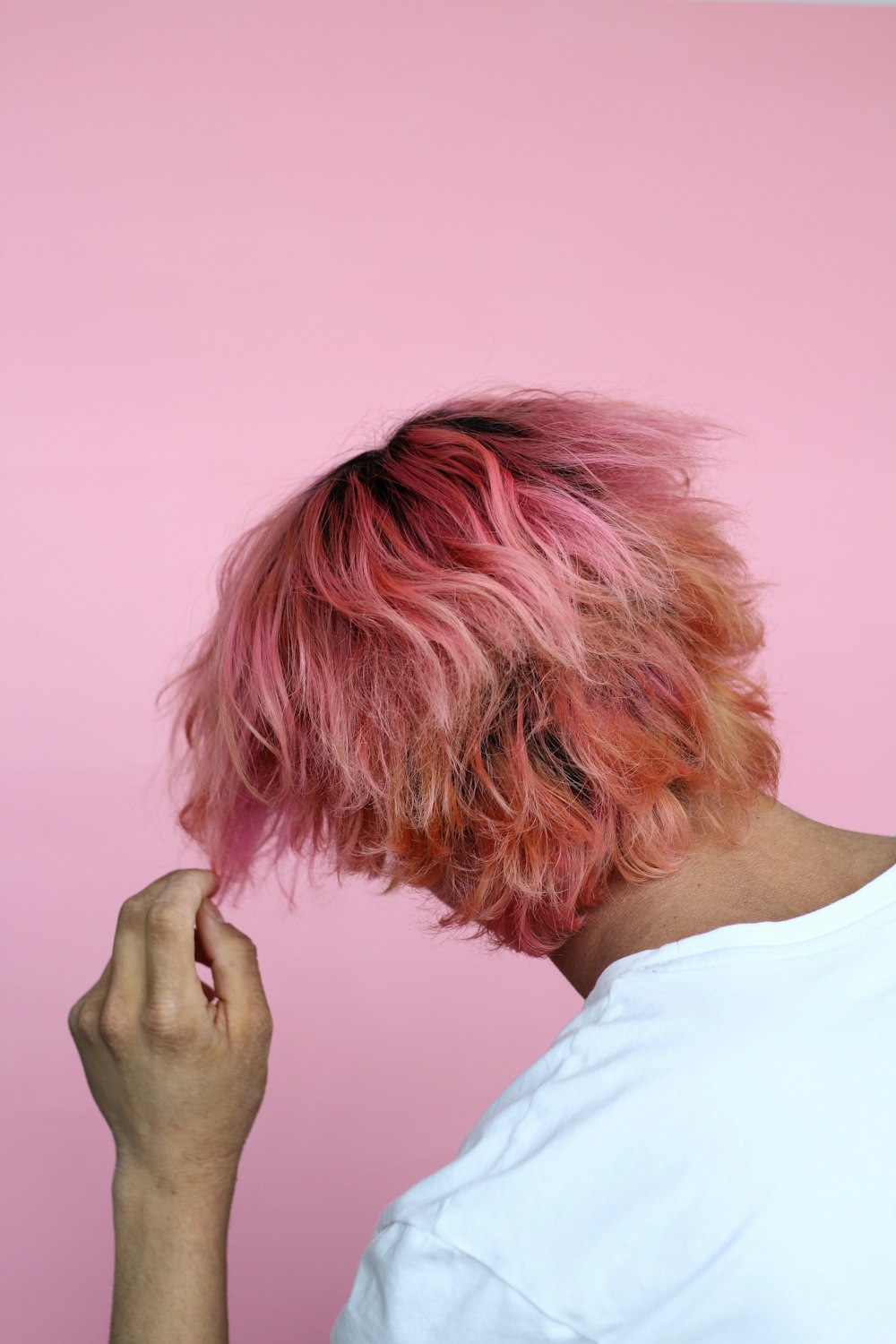 person in white top touch hair with pink dye