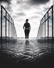 grayscale photo of woman in between gray metal railings
