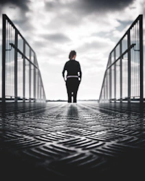 grayscale photo of woman in between gray metal railings