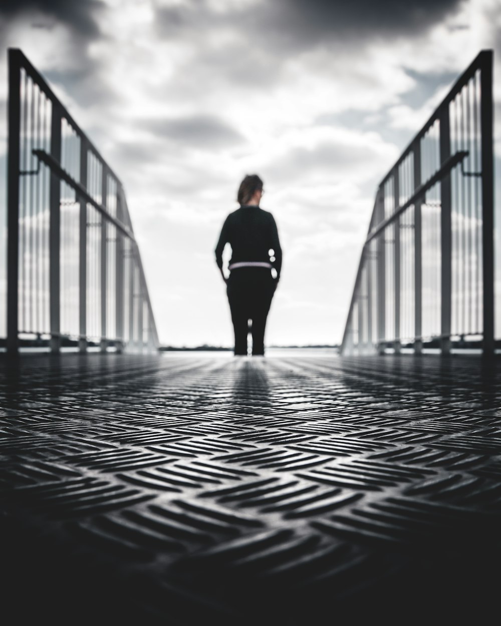 grayscale photo of woman in between gray metal railings