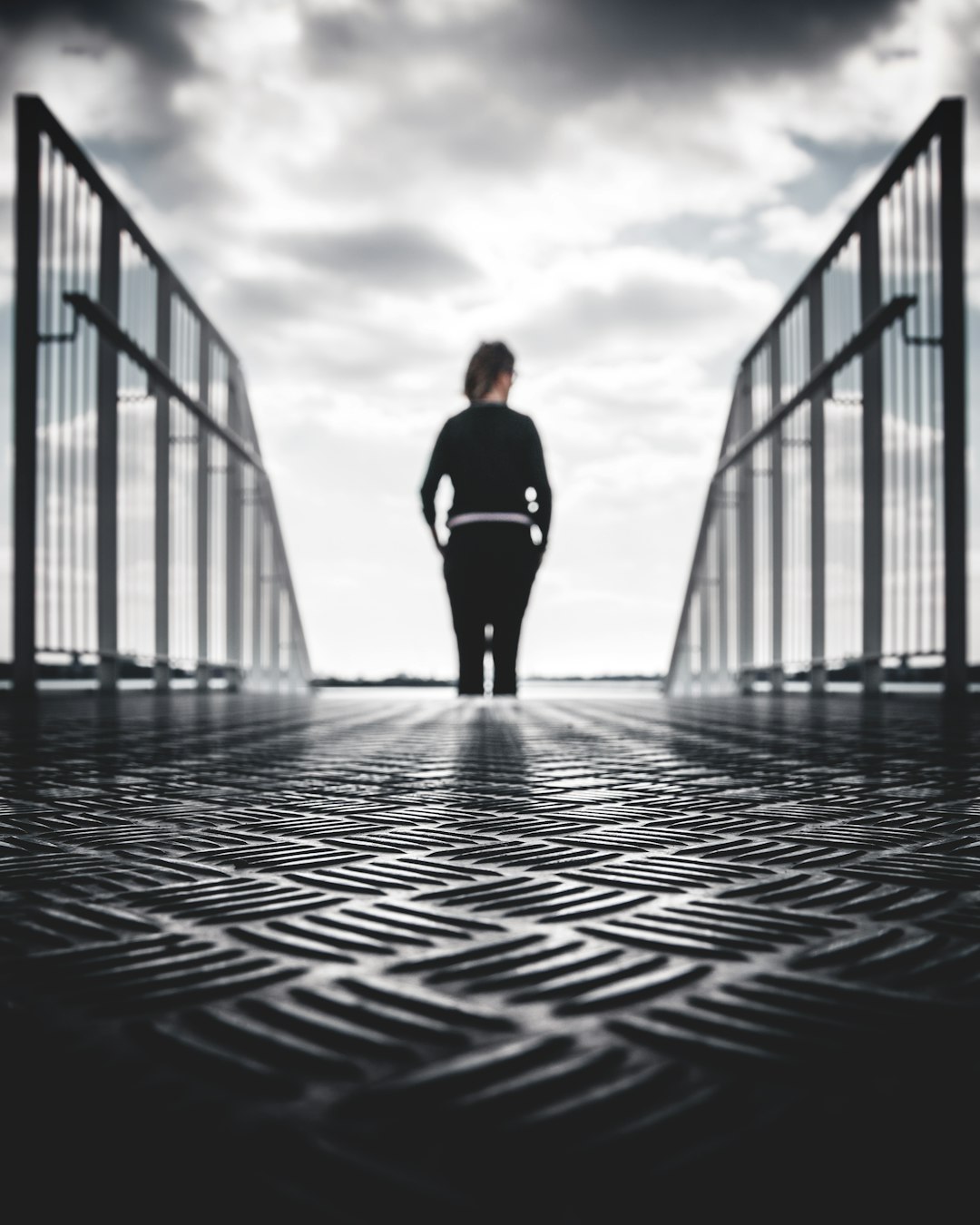 grayscale photo of woman in between gray metal railings