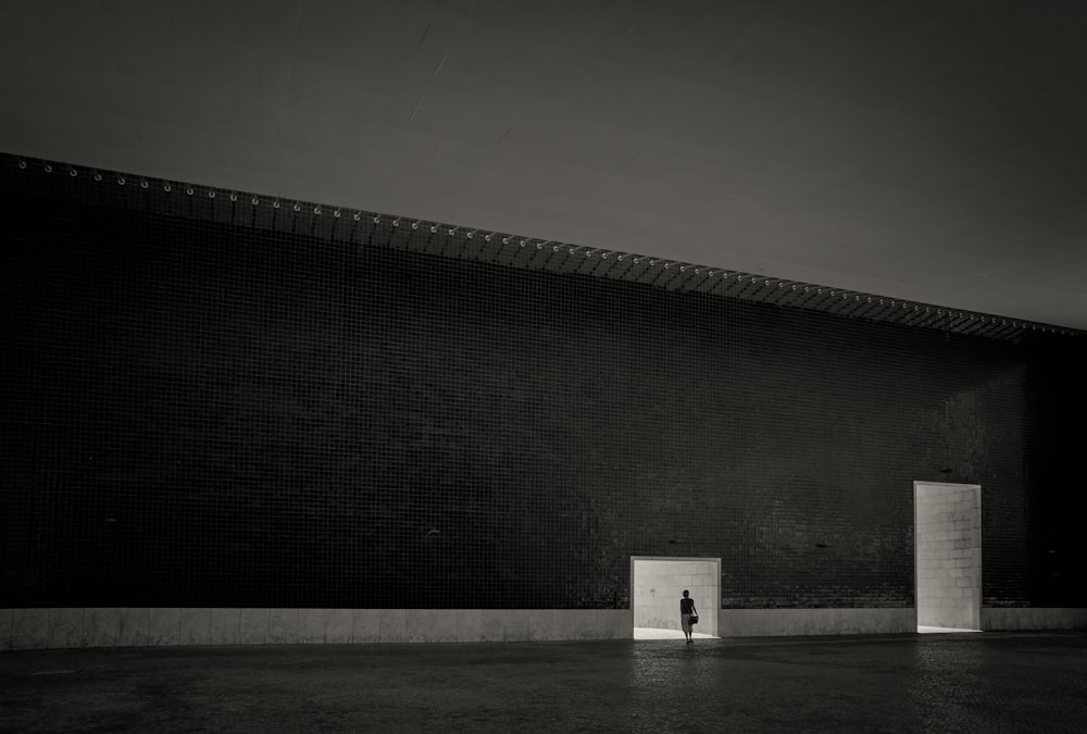 person standing in front of small tunnel beside of big tunnel grayscale photography