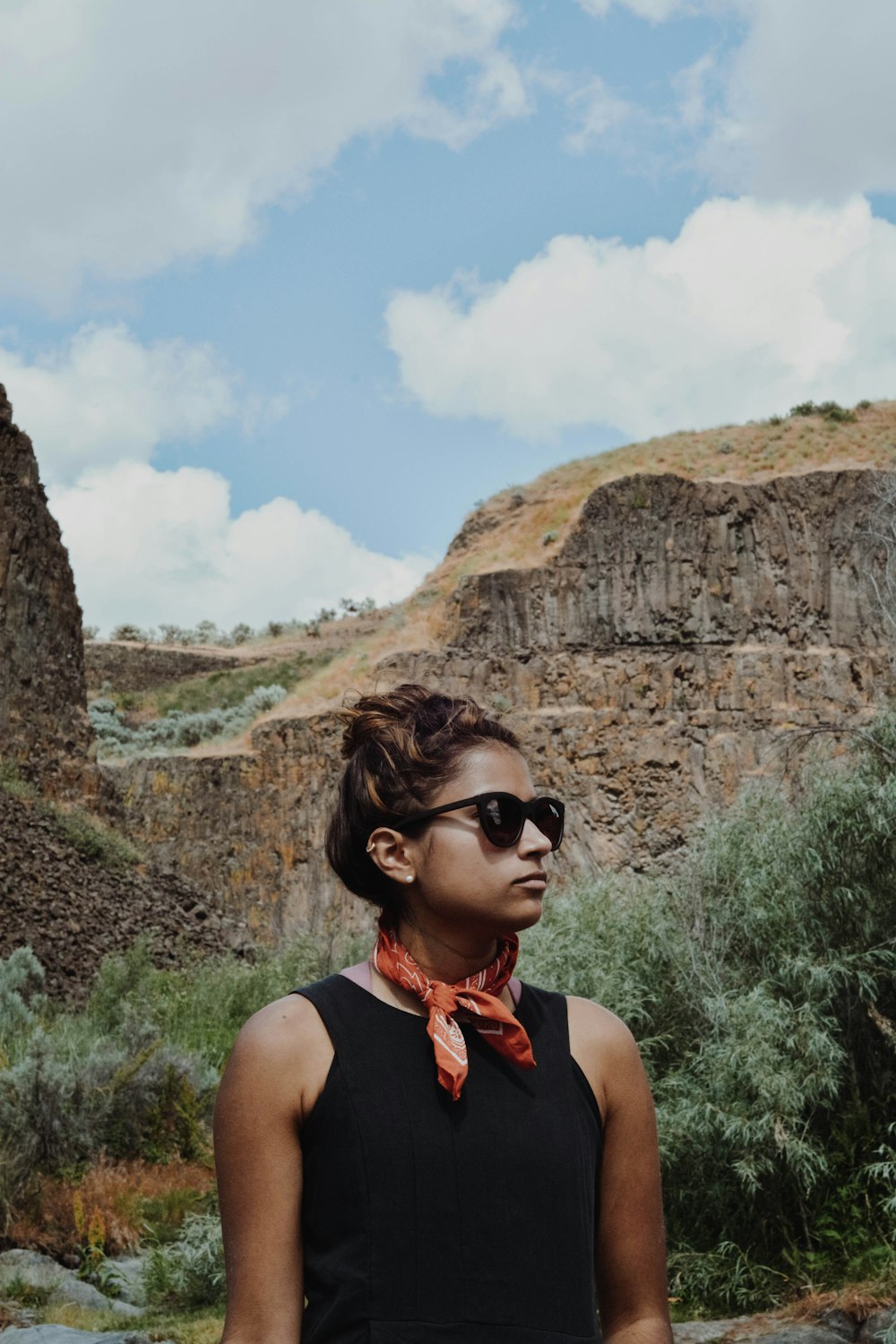 woman wearing black tank top stands beside brown cliff under blue sky during daytime