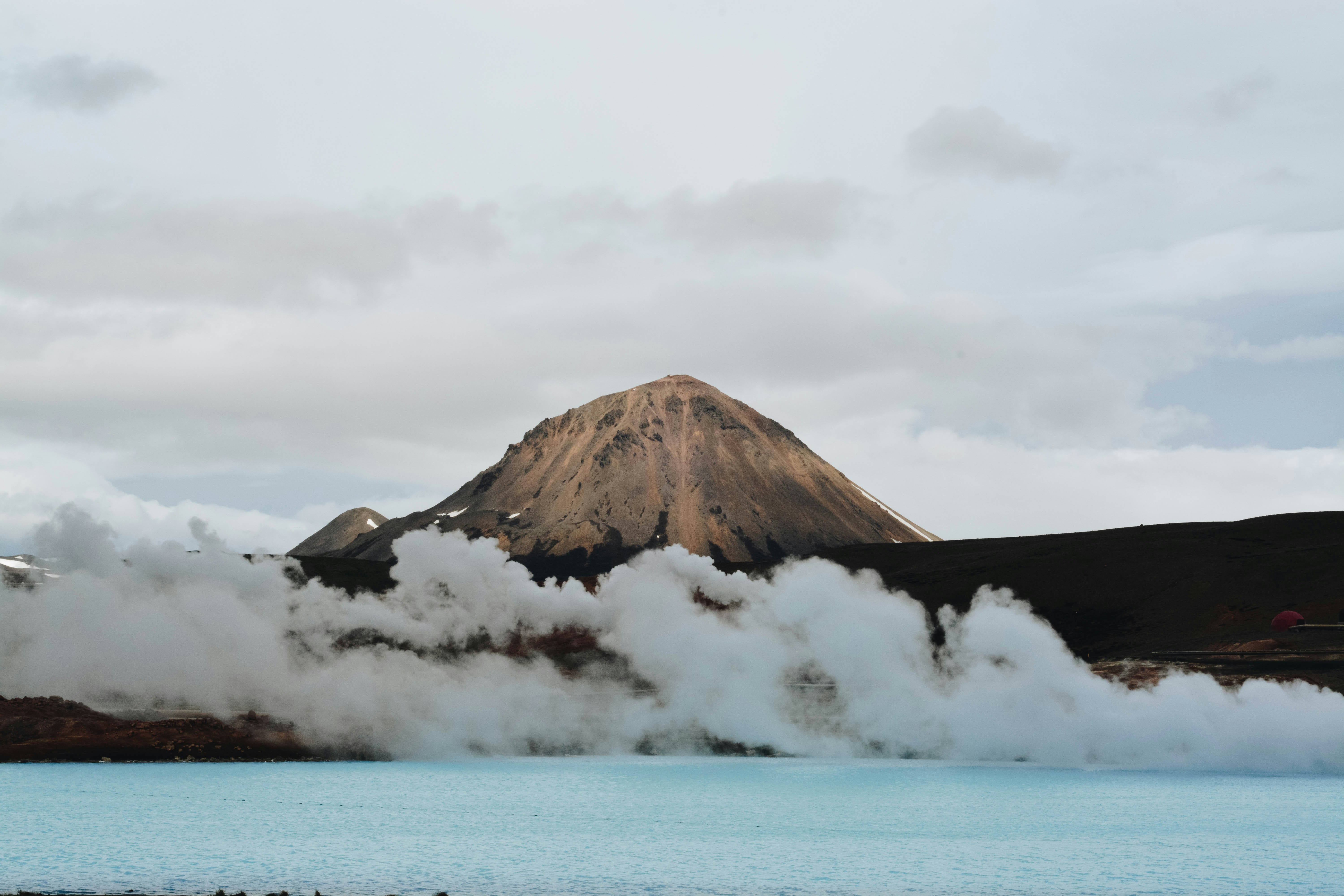 body of water in front of brown mountain with white clouds during daytime, 
