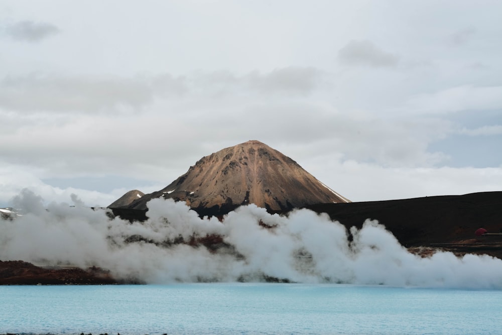 body of water in front of brown mountain with white clouds during daytime