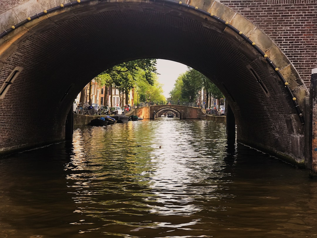 brown concrete bridge over river during daytime, I captured this short of Amsterdam’s beautiful<p></figure>Waterways and bridges while taking a canal tour. I loved the straight aways that were full of bridges upon bridges! The warm colors and reflective water were incredible.