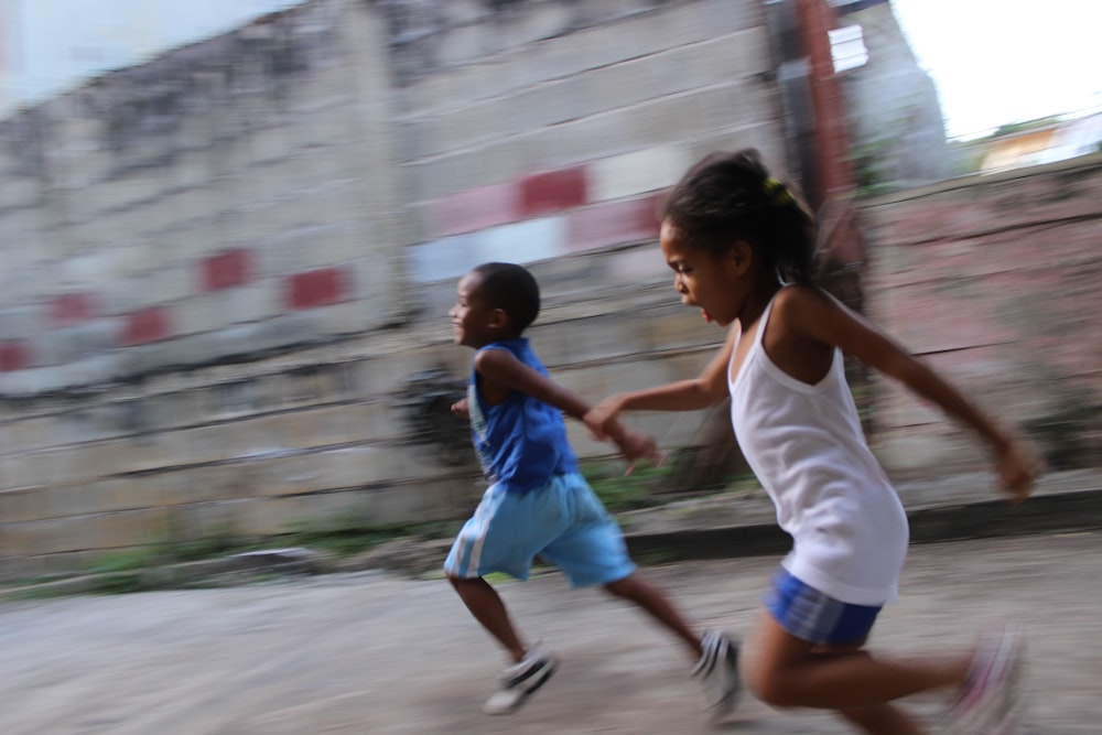 灰色の壁の横を走る2人の女の子と男の子