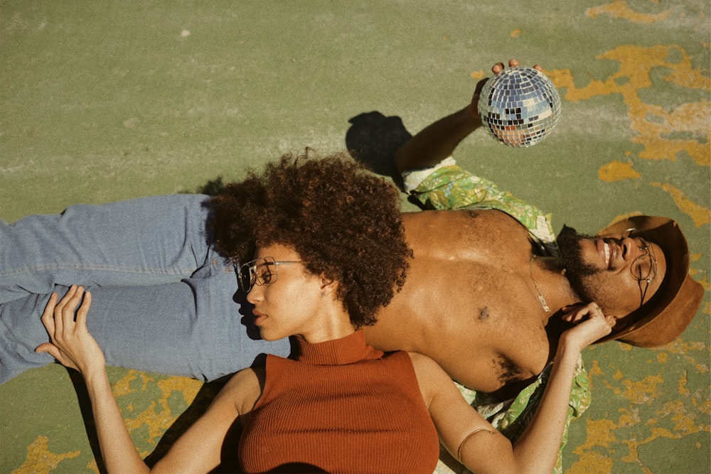 Femme en haut sans manches à col roulé marron allongée sur le ventre de l’homme portant une chemise verte à col boutonné tenant une boule disco