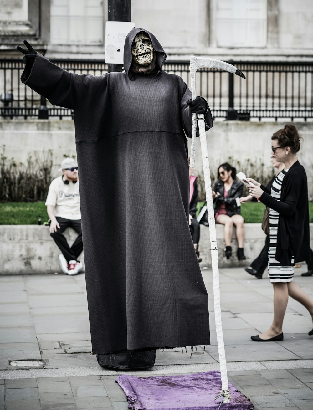 Homme en costume de faucheuse avec faux près de la femme marchant et des gens assis sur le rebord